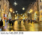 SAINT PETERSBURG, RUSSIA-December 25, 2023: People walking along Bolshaya Morskaya Street decorated with garlands and Christmas trees near arch of General Staff Building in New Year holidays. Редакционное фото, фотограф Виктория Катьянова / Фотобанк Лори