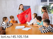 Group of curious preteen learners and young female teacher with flag of Morocco in classroom of academy. Стоковое фото, фотограф Яков Филимонов / Фотобанк Лори