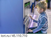 A boy interacts with an interactive screen at an exhibit. Copy space. Стоковое фото, фотограф Алла Чесноковва / Фотобанк Лори