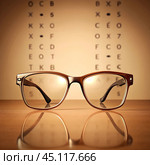A pair of eyeglasses is placed in front of a vision test chart, symbolizing clear vision and eye health, with a warm-toned background. Стоковое AI-изображение, AI-художник Ольга Игнашина / Фотобанк Лори