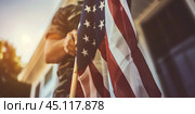 Man holding an American flag in front of a house, symbolizing patriotism, national pride, and respect for the United States. Стоковое AI-изображение, AI-художник Anastacia Gaikova / Фотобанк Лори