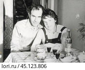 Мужчина обнимает женщину за плечи, сидя за кухонным столом с чайными чашками и бутылкой молдавского кагора "Чумай". Середина 1970-х годов. Стоковое фото, фотограф Retro / Фотобанк Лори