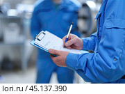 A warehouse worker in a blue jumpsuit checks the goods for shipment on an invoice on a tablet. Стоковое AI-изображение, AI-художник Ярославский Максим / Фотобанк Лори