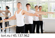 Sports young guy in black and white sportswear, participating 2nd position of ballet stance at barre with group in choreography studio. Стоковое фото, фотограф Яков Филимонов / Фотобанк Лори