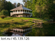 House-Museum of A. P. Hannibal with a reflection in the pond in the Petrovskoye estate of the natural landscape Reserve of A. S. Pushkin on a sunny summer day, Pushkinskie Gory, Pskov region, Russia. Редакционное фото, фотограф Ula Ulachka / Фотобанк Лори
