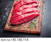 Raw meat, beef steak with seasoning on chopping board on dark background with rosemary, Стоковое фото, фотограф Natalia Gdovskaia / Фотобанк Лори