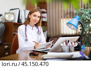 Young female general practitioner studies the patient's outpatient card, writing down the appointment. Стоковое фото, фотограф Яков Филимонов / Фотобанк Лори