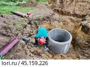 Worker chisels out hole for sewer pipe in concrete septic tank ring using hammer drill with chisel. Стоковое фото, фотограф Владимир Григорьев / Фотобанк Лори
