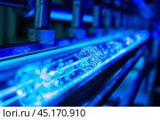 Water bottles being sterilized with ultraviolet light on conveyor belt. Стоковое AI-изображение, AI-художник Иван Рябоконь / Фотобанк Лори