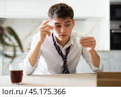 Sick young man with hangover drinks pills while sitting at table. Стоковое фото, фотограф Яков Филимонов / Фотобанк Лори