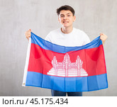 Happy young man holding flag of Cambodia against unicoloured background. Стоковое фото, фотограф Яков Филимонов / Фотобанк Лори