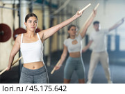 Slender girl, together with other athletes, does a warm-up using a long stick in gym. Стоковое фото, фотограф Яков Филимонов / Фотобанк Лори