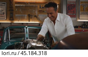 Mechanic smiling while repairing a classic car engine in the garage. Стоковое AI-видео, аниматор Юрий Поздников / Фотобанк Лори