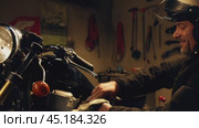 Motorcycle mechanic working late in garage on a project bike. Стоковое AI-видео, аниматор Юрий Поздников / Фотобанк Лори