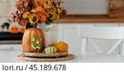 A vase of flowers,a jack pumpkin and candles on a tray. In the background - the interior of a white kitchen in Scandi style. The concept of home and comfort. Autumn decor for the Halloween holiday. Стоковое фото, фотограф Photojuli / Фотобанк Лори
