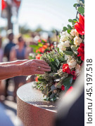 Senior woman paying respects at memorial with flowers and crowd in background. Стоковое AI-изображение, AI-художник Юрий Поздников / Фотобанк Лори