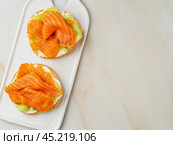 Two open sandwiches with salmon, cream cheese, cucumber slices on white marble table. Стоковое фото, фотограф Natalia Gdovskaia / Фотобанк Лори