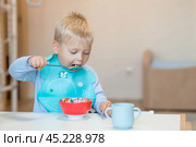 Baby food. Eating. Feeding the baby. A cute kid eats on his own with a spoon. Healthy eating. Family and children. Стоковое фото, фотограф Photojuli / Фотобанк Лори
