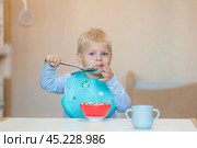 Baby food. Eating. Feeding the baby. A cute kid eats on his own with a spoon. Healthy eating. Family and children. Стоковое фото, фотограф Photojuli / Фотобанк Лори