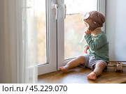 A cute 2-year-old boy in a cap is playing on the windowsill with a wooden airplane. Children's wooden toys for child development. Стоковое фото, фотограф Photojuli / Фотобанк Лори