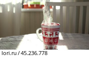 Steaming Cup of Coffee or Tea on Table. White linen Tablecloth. Close up ceramic red Christmas mug with smoke on old table in dining room interior background. Hot Drink Concept. Cozy Morning. Стоковое видео, видеограф Марина Демидюк / Фотобанк Лори