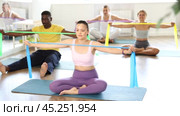 Focused young Asian woman performing rear delt pulls using resistance band with group of men and women of different nationalities in cozy sunlit fitness studio. Стоковое видео, видеограф Яков Филимонов / Фотобанк Лори