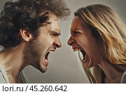 Angry young adult Caucasian woman yelling versus her husband on grey background, Young couple arguing and fighting. Domestic violence and emotional abuse scene of woman and man screaming at each other. Стоковое AI-изображение, AI-художник Sergey Grishin / Фотобанк Лори