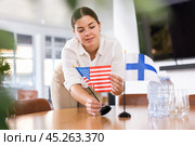 Positive young woman putting flag of the USA on the table with flag of Finland in conference room. Стоковое фото, фотограф Яков Филимонов / Фотобанк Лори