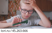 The boy solves math, does homework in the kitchen and yawns from boring tasks. The child writes the answer to the solution of the example in a notebook. The kid sits at the table and performs the task. Стоковое видео, видеограф Екатерина Золина / Фотобанк Лори