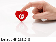 Tunisia flag. Love and respect Tunisia. A man's hand holds a heart in the shape of the Tunis flag on a white glass surface. The concept of patriotism and pride. Стоковое фото, фотограф Никита Бурденков / Фотобанк Лори