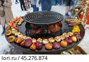 Holiday fair on the street in winter in the city. Cooking vegetables on the grill at the festivities (2024 год). Редакционное фото, фотограф Zima Nadezhda / Фотобанк Лори