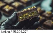 Дубайский шоколад с начинкой из зеленых фисташек в черной перчатке на фоне шоколадных изделий. Стоковое AI-изображение, AI-художник Анна Чижова / Фотобанк Лори