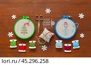 Winter needlework. Cross stitch Christmas tree and snowman in hoop and embroidery accessories on wooden background. Space for text on top. Handmade gifts concept. Flat lay, close-up, top view, mock up. Стоковое фото, фотограф Виктория Катьянова / Фотобанк Лори