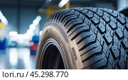 Car tire showcased in auto repair shop. Focus on intricate tread design, indicating strong grip and safety. Workshop tools and machinery present in backdrop. Стоковое AI-изображение, AI-художник Павел Муравьев / Фотобанк Лори