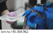 The stylist applies blue dye to a strand and carefully wraps it in foil for the best results. Стоковое AI-видео, аниматор Юрий Поздников / Фотобанк Лори