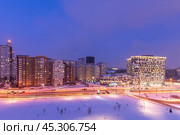 Winter evening in a modern city reveals a snowy landscape with glimmering lights from contemporary buildings and busy streets, creating a lively atmosphere. Стоковое фото, фотограф Алексей Климкин / Фотобанк Лори