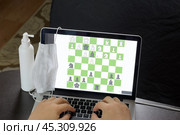 A man solves a chess problem online. Chess board with figures on a laptop screen. Leisure in self-isolation, in the twilight. International chess day. Стоковое фото, фотограф Vadzim Yakubovich / Фотобанк Лори