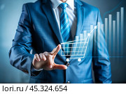 A businessman touches a virtual sales volume screen and shopping cart for a growing online sales business. A summary of the growth of online sales or the increase in the price of a grocery basket. Стоковое AI-изображение, AI-художник Photojuli / Фотобанк Лори