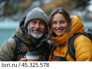 Couple in nature, dressed in warm jackets. The man in a hat and a khaki jacket, and the woman in a bright yellow jacket. Both are holding mugs with hot drinks in their hands, enjoying the fresh air. Their smiles express joy and satisfaction with the moment, which makes the photo warm and inspiring. The photo is perfect for themes related to active recreation, travel and autumn walks. Стоковое AI-изображение, AI-художник Анна Кривицкая / Фотобанк Лори