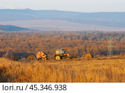 Beautiful rural landscape. The tractor drives across the field and collects mowed hay into stacks. Hills in the distance. Agriculture in the countryside. Haymaking. Стоковое фото, фотограф Андрей Степанов / Фотобанк Лори