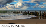 Waves gently lapping against wooden posts on a serene sandy beach under a vibrant sky near the coastline. Стоковое фото, фотограф Долотова Елена Викторовна / Фотобанк Лори