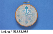 Video of hand embroidered cross stitch snowflake in wooden hoop on blue background. Winter craft, needlework and Christmas gifts concept. Cross stitches as a hobby. Flat lay, ccose-up. Стоковое видео, видеограф Виктория Катьянова / Фотобанк Лори