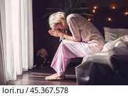 Unhappy sad middle aged woman sitting on bed at home. Стоковое фото, фотограф Гладских Татьяна / Фотобанк Лори