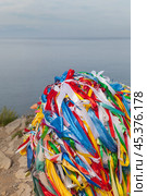 Baikal Lake. The tip of Olkhon Island - northern cape Khoboy attracts many tourists, according to tradition they tie colored ribbons to serge pole. Many colored satin ribbons against background of lake water (2024 год). Стоковое фото, фотограф Виктория Катьянова / Фотобанк Лори