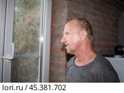 A man soaked in the rain stands near the window and looks at the bad weather in autumn. Стоковое фото, фотограф Коханова Наталья / Фотобанк Лори