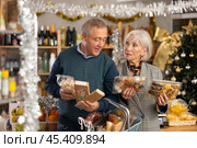 Elderly couple choosing products for Christmas table in supermarket - nougat, marzipan, panellets and other sweets. Стоковое фото, фотограф Яков Филимонов / Фотобанк Лори