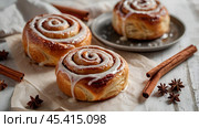 The cinnabons. Close-up of cinnamon buns. Beautiful buns with fresh cinnamon and icing on a wooden table. Fragrant homemade New Year's pastries. Стоковое AI-изображение, AI-художник Photojuli / Фотобанк Лори