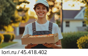Smiling delivery woman holding pizza box at sunset in residential area. Стоковое AI-видео, аниматор Юрий Поздников / Фотобанк Лори