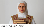 Ближневосточная женщина в традиционной скромной одежде держит книги для культурного образования. Стоковое AI-изображение, AI-художник ФотоИнтеллект / Фотобанк Лори