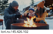 A family warms up by a fire pit on a snowy winter day. Стоковое AI-изображение, AI-художник Сергей Толмачёв / Фотобанк Лори